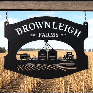 May include: A black metal sign hanging from chains, featuring the text "BROWNLEIGH FARMS EST 2017" above a cutout silhouette of a farm scene with a combine harvester, two grain silos, a tractor, and rows of crops in a field.