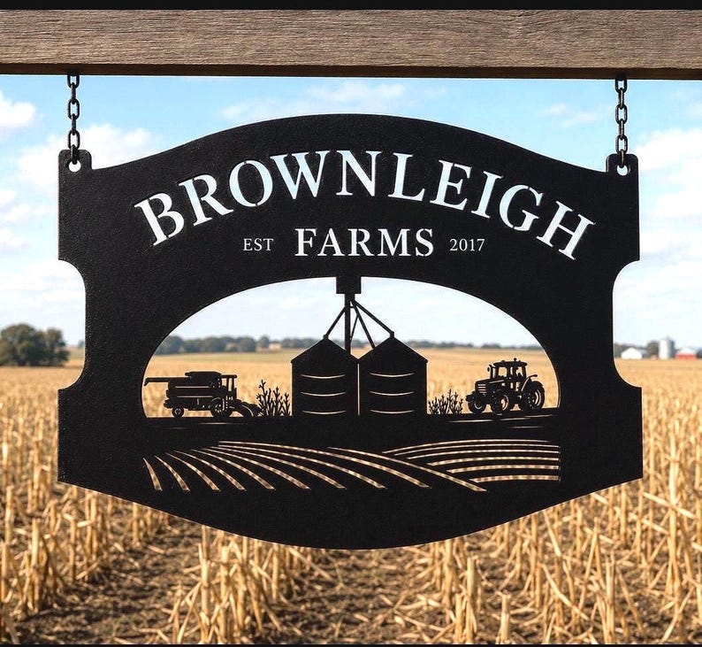May include: A black metal sign hanging from chains, featuring the text "BROWNLEIGH FARMS EST 2017" above a cutout silhouette of a farm scene with a combine harvester, two grain silos, a tractor, and rows of crops in a field.