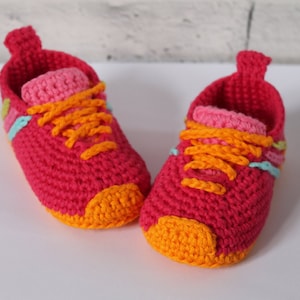 May include: A pair of pink crocheted baby shoes with orange laces and yellow toes.