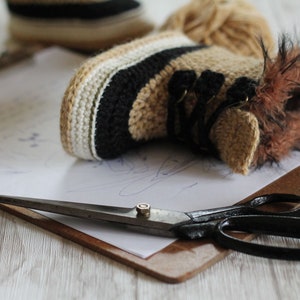 May include: A pair of crocheted baby booties with brown fur trim, a pair of scissors, and a piece of paper on a clipboard.