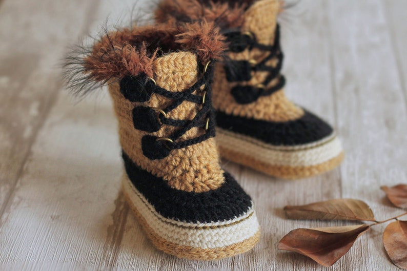 May include: A pair of crocheted baby booties with brown and black yarn, featuring a faux fur trim and a lace-up design.