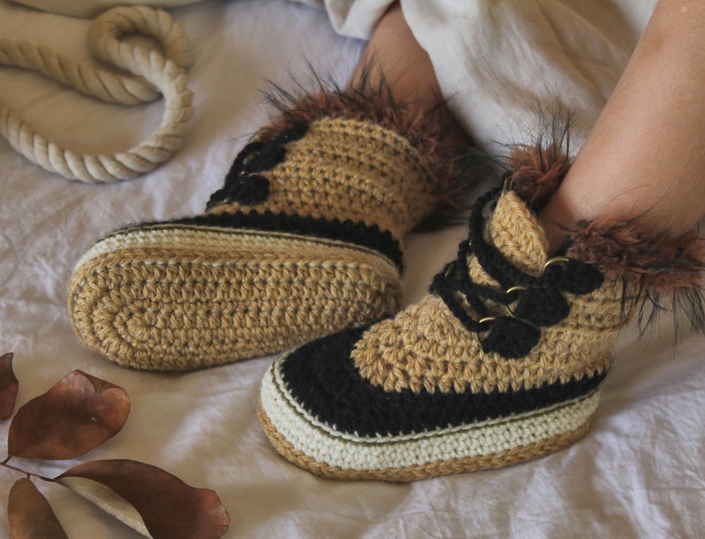 May include: Crocheted tan and black slippers with faux fur trim. The slippers have a lace-up design with black laces and gold-colored eyelets.
