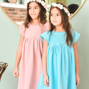 May include: Two young girls wearing flower crowns and matching dresses. The girl on the left is wearing a pink dress and the girl on the right is wearing a blue dress.