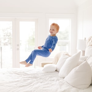 Little boy in blue organic cotton pajamas jumps on the bed