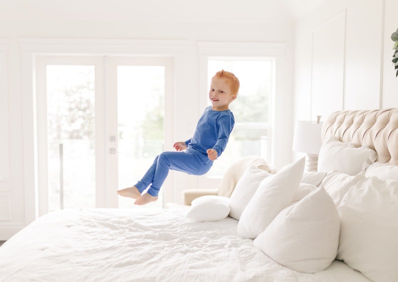 Little boy in blue organic cotton pajamas jumps on the bed