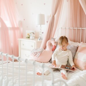 Little girl in white organic cotton pajamas sits on bed reading book