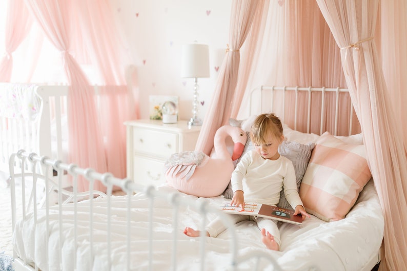 Little girl in white organic cotton pajamas sits on bed reading book