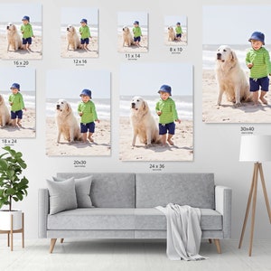 Op de afbeelding: Een jonge jongen in een groen-wit gestreept shirt en blauwe broek staat op een strand met een witte hond. De jongen draagt een blauwe pet en de hond kijkt naar de camera.