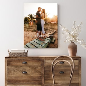 May include: A wedding welcome sign with a photo of a couple on a wooden dock. The sign says "Welcome" with the couple's names and wedding date, "June 26, 2021".