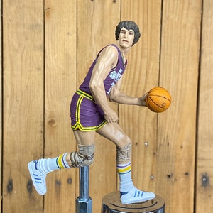May include: A purple and gold basketball player figurine holding a basketball. The figurine is mounted on a chrome beer tap.