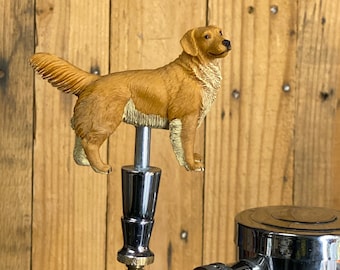 Könnte beinhalten: Eine Golden-Retriever-Hundefigur auf einem verchromten Bierhahn. Der Hahn ist an einem verchromten Bierzapfhahn befestigt.