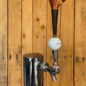 Puede incluir: Un tirador de grifo de cerveza personalizado con un dise&ntilde;o de cabeza de palo de golf. El mango es de madera y material negro, con una pelota de golf y el logotipo de Guinness. El grifo es cromado y est&aacute; montado en una columna de acero inoxidable.