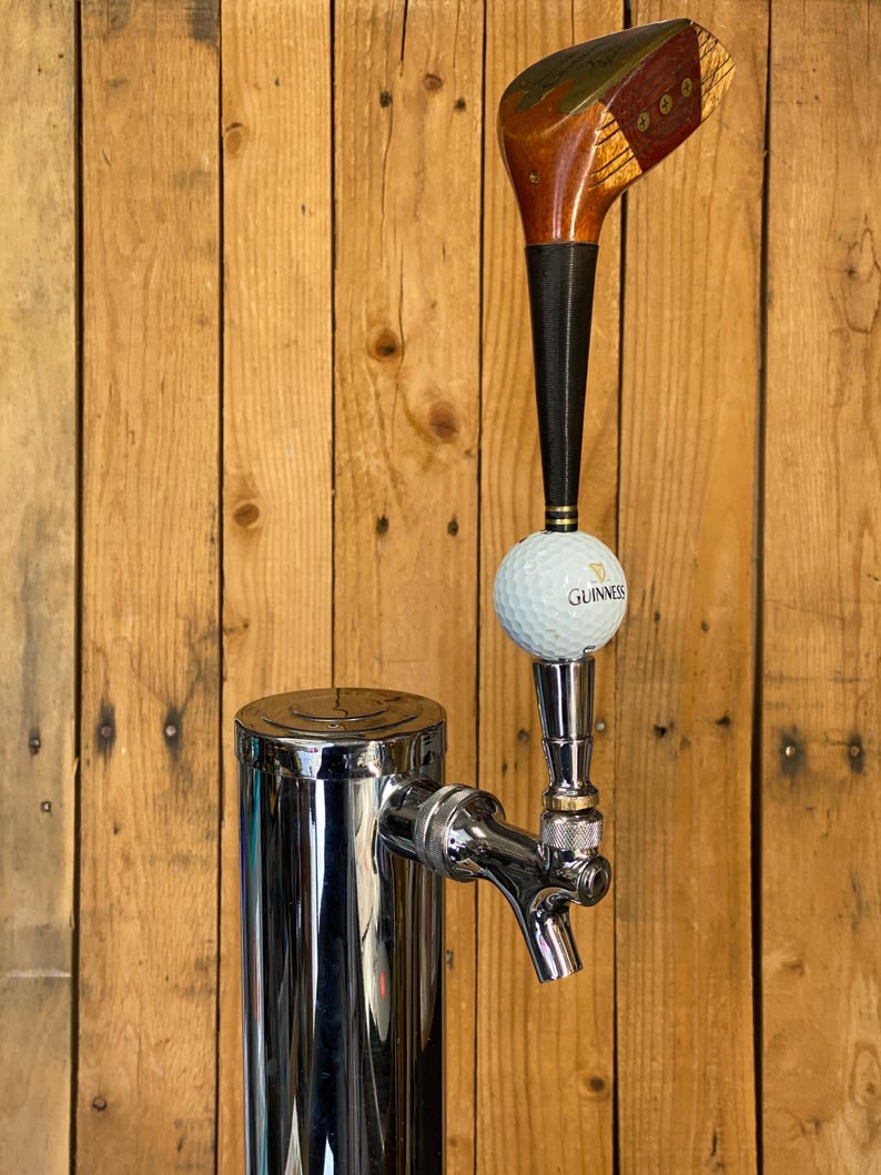 Puede incluir: Un tirador de grifo de cerveza personalizado con un dise&ntilde;o de cabeza de palo de golf. El mango es de madera y material negro, con una pelota de golf y el logotipo de Guinness. El grifo es cromado y est&aacute; montado en una columna de acero inoxidable.
