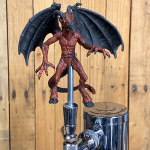 May include: A red and black demon figurine with wings, used as a beer tap handle.
