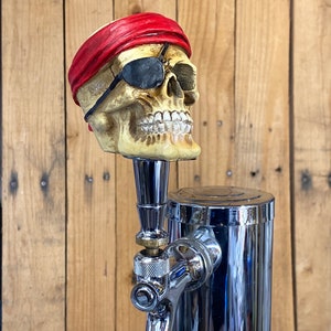 May include: A chrome beer tap with a skull-shaped handle. The skull is wearing a red bandana and an eye patch.