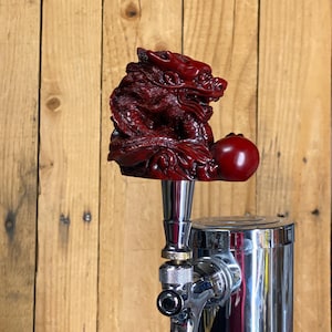 May include: A red dragon beer tap handle with a red orb in its claws. The handle is attached to a chrome beer tap.