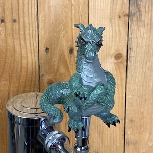 May include: Green dragon beer tap handle with a detailed design. The dragon is sitting with its wings folded and has a fierce expression.