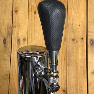 May include: A black beer tap handle with a textured, dimpled surface attached to a polished chrome faucet assembly. The handle features a tapered, ergonomic shape and is mounted onto a cylindrical chrome beer tower base with a metallic finish.
