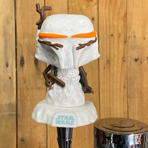 May include: A white, glittery snowman-themed Boba Fett Star Wars beer tap handle with orange and brown accents. The handle has the words "Star Wars" printed on the base.
