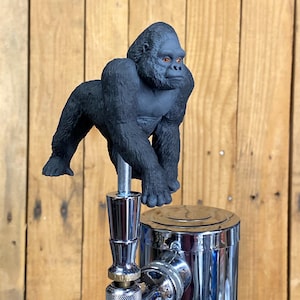 May include: A black gorilla figurine beer tap handle. The gorilla is in a walking pose with its head turned to the side. The tap handle is made of metal and has a chrome finish.