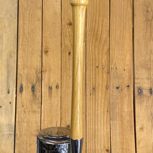 May include: A light brown wooden baseball bat handle attached to a vertical chrome metal beer tap faucet. The handle features a smooth, polished finish with visible wood grain patterns, extending upward from the metallic base hardware.