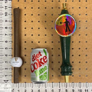 May include: A collection of items: a brown golf club grip with a Guinness golf ball, a Diet Coke Lime can, and a green tap handle with the text "Tap Daddy Handles.com".