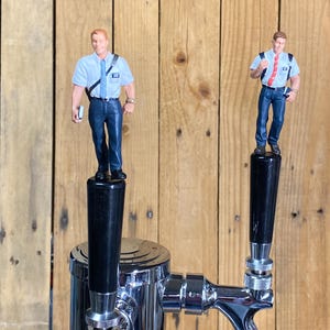 May include: Two chrome beer tap handles with black handles and figurines of men wearing blue shirts and ties on top.