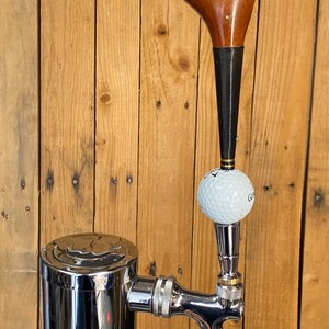 Puede incluir: Un grifo de cerveza personalizado con una cabeza de palo de golf vintage y una pelota de golf. El grifo es de cromo pulido y est&aacute; montado en una torre de acero inoxidable. Se puede ver el texto "Powerbilt Citation".
