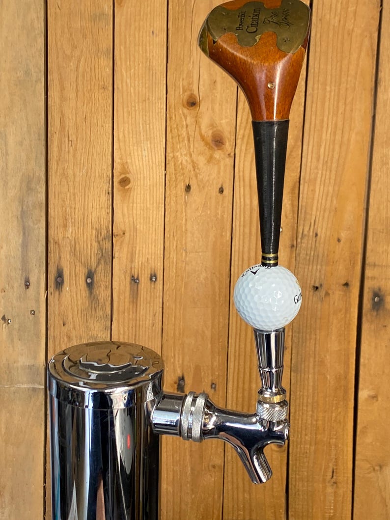 Puede incluir: Un grifo de cerveza personalizado con una cabeza de palo de golf vintage y una pelota de golf. El grifo es de cromo pulido y est&aacute; montado en una torre de acero inoxidable. Se puede ver el texto "Powerbilt Citation".