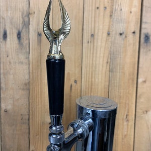 May include: A black and gold beer tap handle with an eagle design. The handle is made of wood and metal.