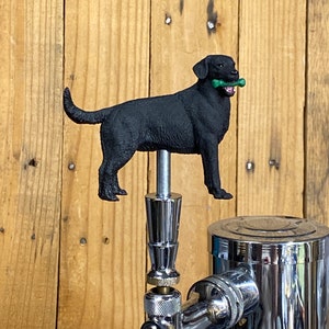 May include: Black Labrador Retriever dog beer tap handle with a green bone in its mouth.