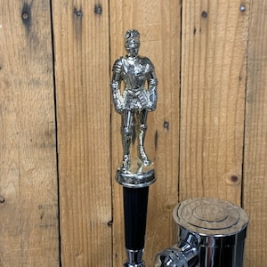 May include: A silver knight figurine on top of a black and chrome beer tap.