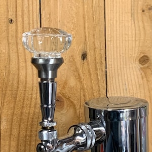 May include: A chrome beer tap with a clear glass knob on top. The tap is attached to a chrome beer keg.