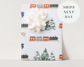 May include: Blue and white wrapping paper with a repeating pattern of red train cars, pine trees, and white stars. The paper is decorated with a white bow.
