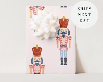 May include: A wrapped gift with a white bow. The wrapping paper is light pink and features a repeating pattern of toy nutcracker soldiers in red, blue, and pink. The gift is ready to be given.