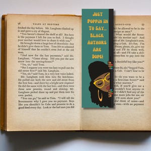 May include: A teal blue bookmark with a black and white illustration of a woman wearing glasses and a black hat. The text on the bookmark reads "Just Poppin' In To Say... Black Authors Are Dope!"