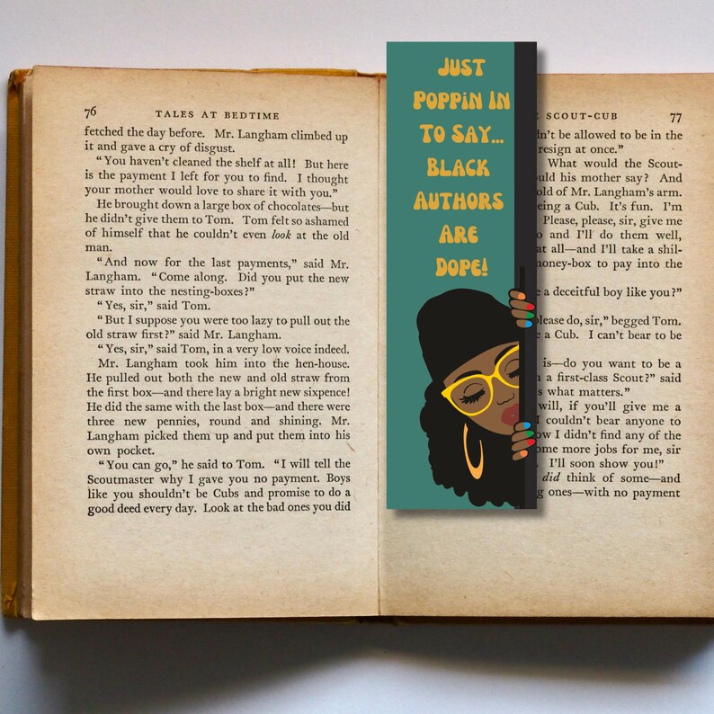 May include: A teal blue bookmark with a black and white illustration of a woman wearing glasses and a black hat. The text on the bookmark reads "Just Poppin' In To Say... Black Authors Are Dope!"
