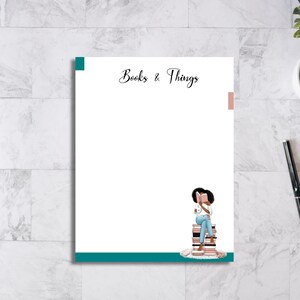 May include: A teal and pink notepad with the text "Books & Things" at the top. A black woman is illustrated sitting on a stack of books, reading a book.