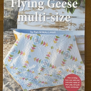 May include: A book cover titled "Flying Geese multi-size" by Pam & Nicky Lintott. The cover features a light blue quilt with colorful triangle patterns. Text on the cover states that over 350,000 copies of their jelly roll quilt books have been sold worldwide.