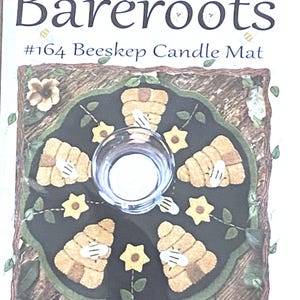 May include: A candle mat with a central glass holder, surrounded by a dark green border with yellow flowers and bee skep designs. The text "Bareroots" and "#164 Beeskeep Candle Mat" are visible.