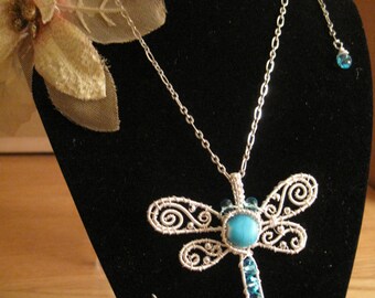 May include: A silver necklace with a dragonfly pendant. The dragonfly is made of wire and has a turquoise gemstone in the center. The necklace has a small turquoise gemstone on the end of the chain.
