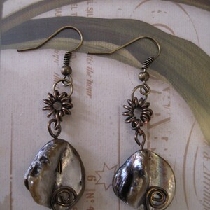 May include: A pair of handcrafted earrings featuring iridescent, shell-shaped pendants. The earrings have bronze-colored hooks, spiral wire accents, and small, flower-shaped embellishments. The earrings are designed for pierced ears.