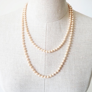 May include: A double-strand pearl necklace on a mannequin. The pearls are a creamy, off-white hue and appear to be of a consistent size. The necklace is draped in a layered style, highlighting its length and design.