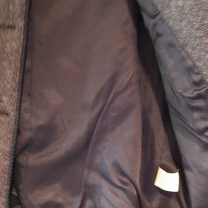 May include: The inside of a gray tweed jacket with a black satin lining. A white tag is sewn into the lining.