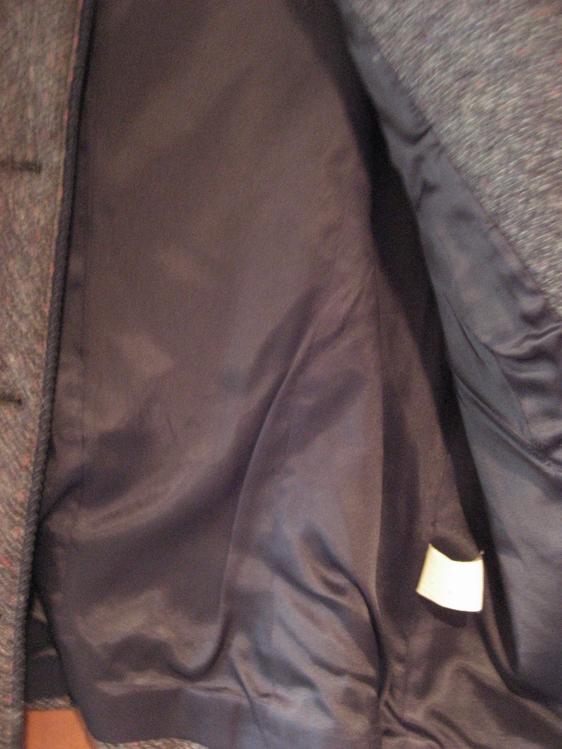 May include: The inside of a gray tweed jacket with a black satin lining. A white tag is sewn into the lining.