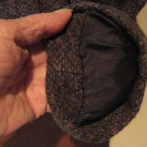 May include: Close-up of a brown tweed fabric with a red and blue flecked pattern. The fabric is folded over to reveal a dark brown lining.