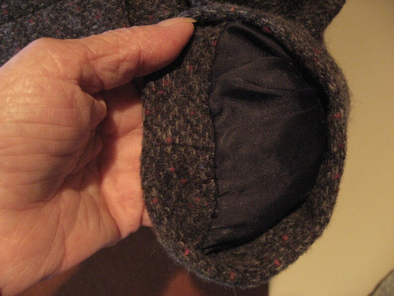 May include: Close-up of a brown tweed fabric with a red and blue flecked pattern. The fabric is folded over to reveal a dark brown lining.