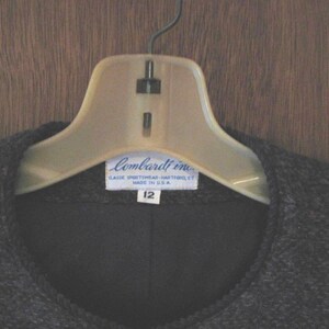 May include: A black sweater with a blue label that reads "Lombardi Inc. Classic Sportswear - Washable - Made in U.S.A." and "12" on a white hanger.