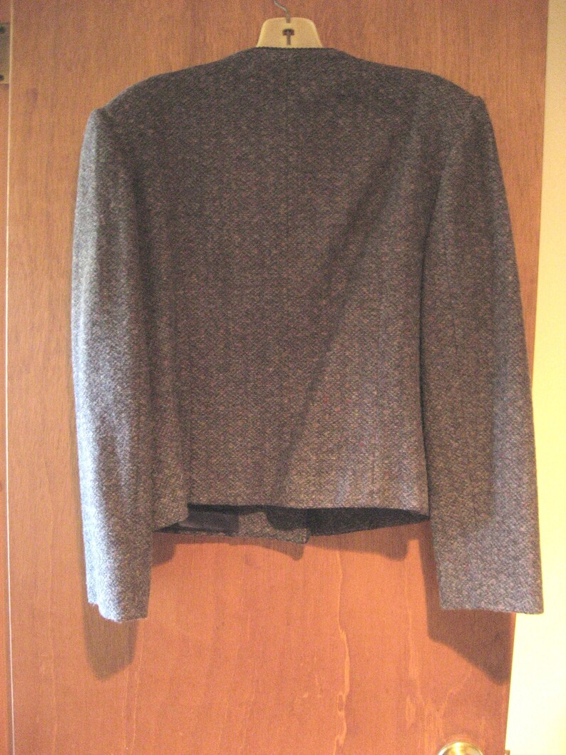 May include: A gray tweed blazer with a classic design. The blazer has a notched collar, long sleeves, and a single button closure.