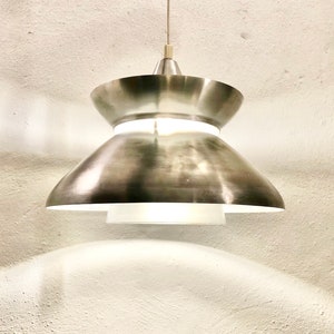 May include: A silver pendant light with a double-tiered shade. The top shade is a flat disc with a slightly curved edge. The bottom shade is a wider, bowl-shaped shade.